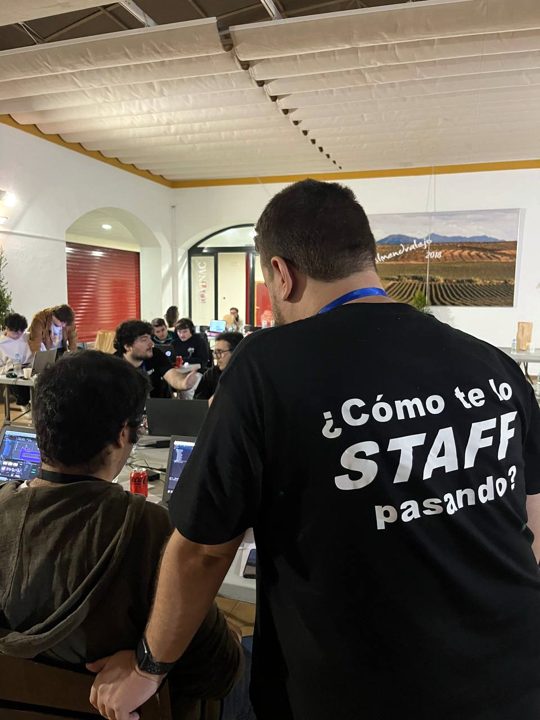 Un miembro del staff con la camiseta «¿Cómo te lo STAFF pasando?» junto a un equipo